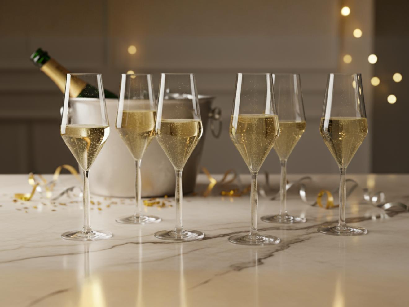 Sechs gefüllte Champagnergläser in Tulpenform mit champagnerfarbigem Stiel stehen auf einem Marmortisch