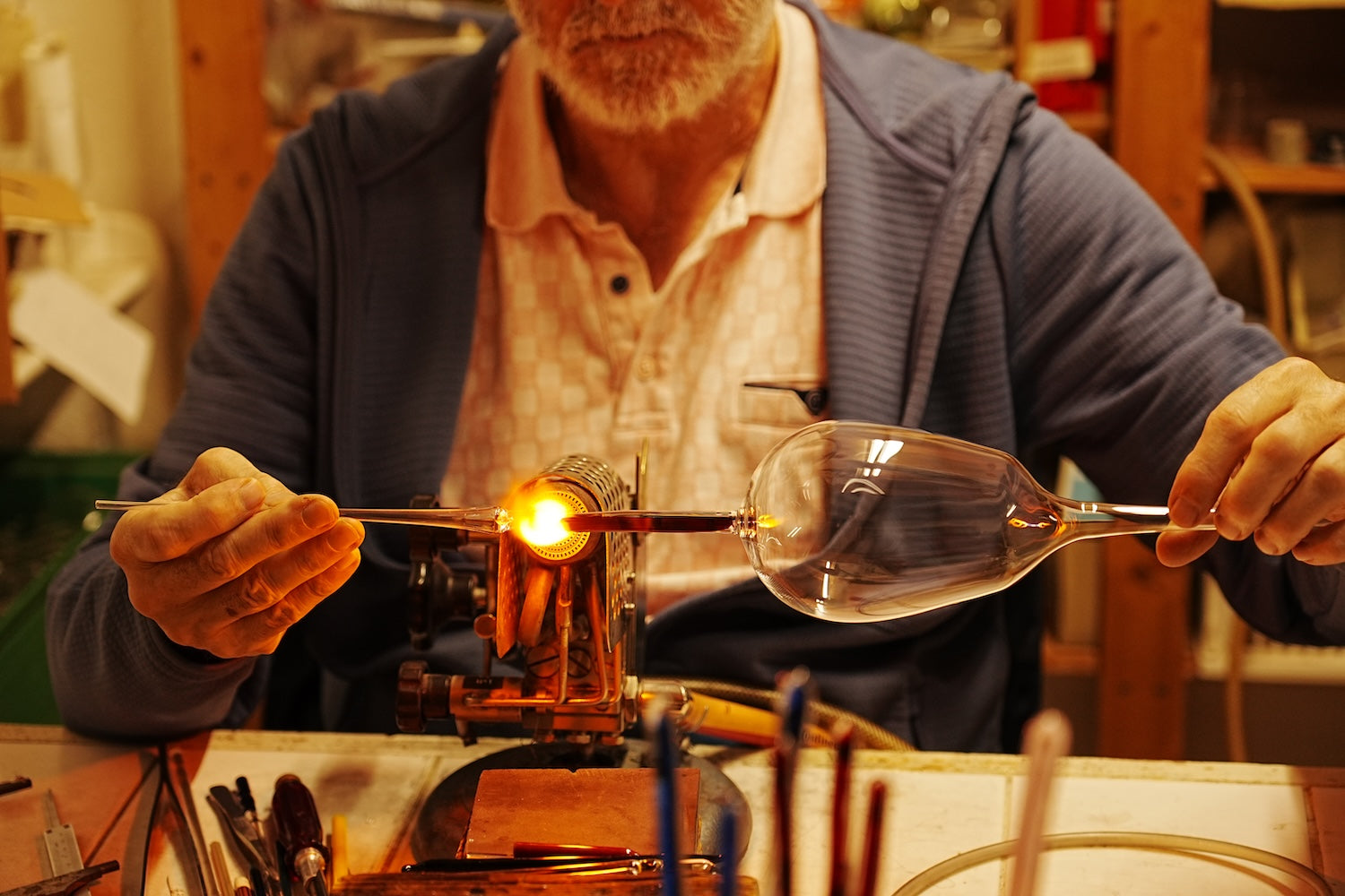 Glasblaeser arbeitet an Rotweinglas vor dem Brenner
