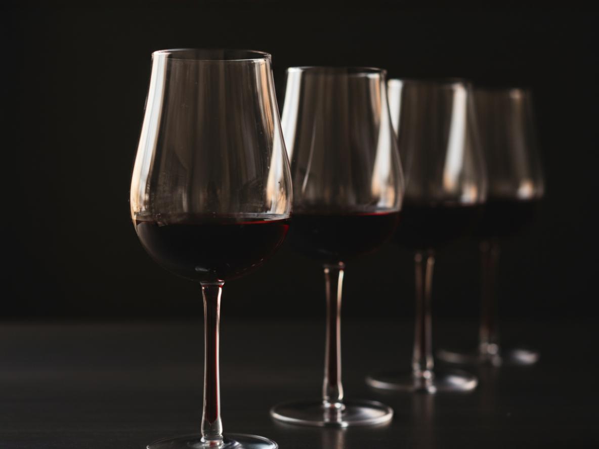 Reihe mit 4 Rotweingläsern gefüllt hintereinander vor schwarzem Hintergrund